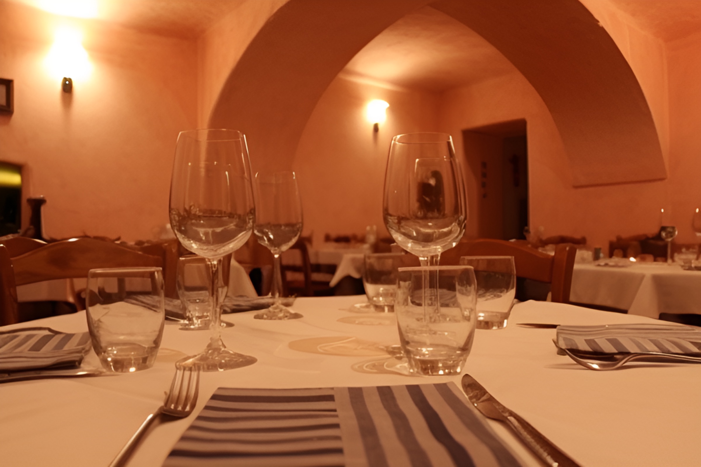 Cucina tipica valdostana: sala dell'Osteria da Nando ad Aosta con tavoli apparecchiati e bicchieri di vino